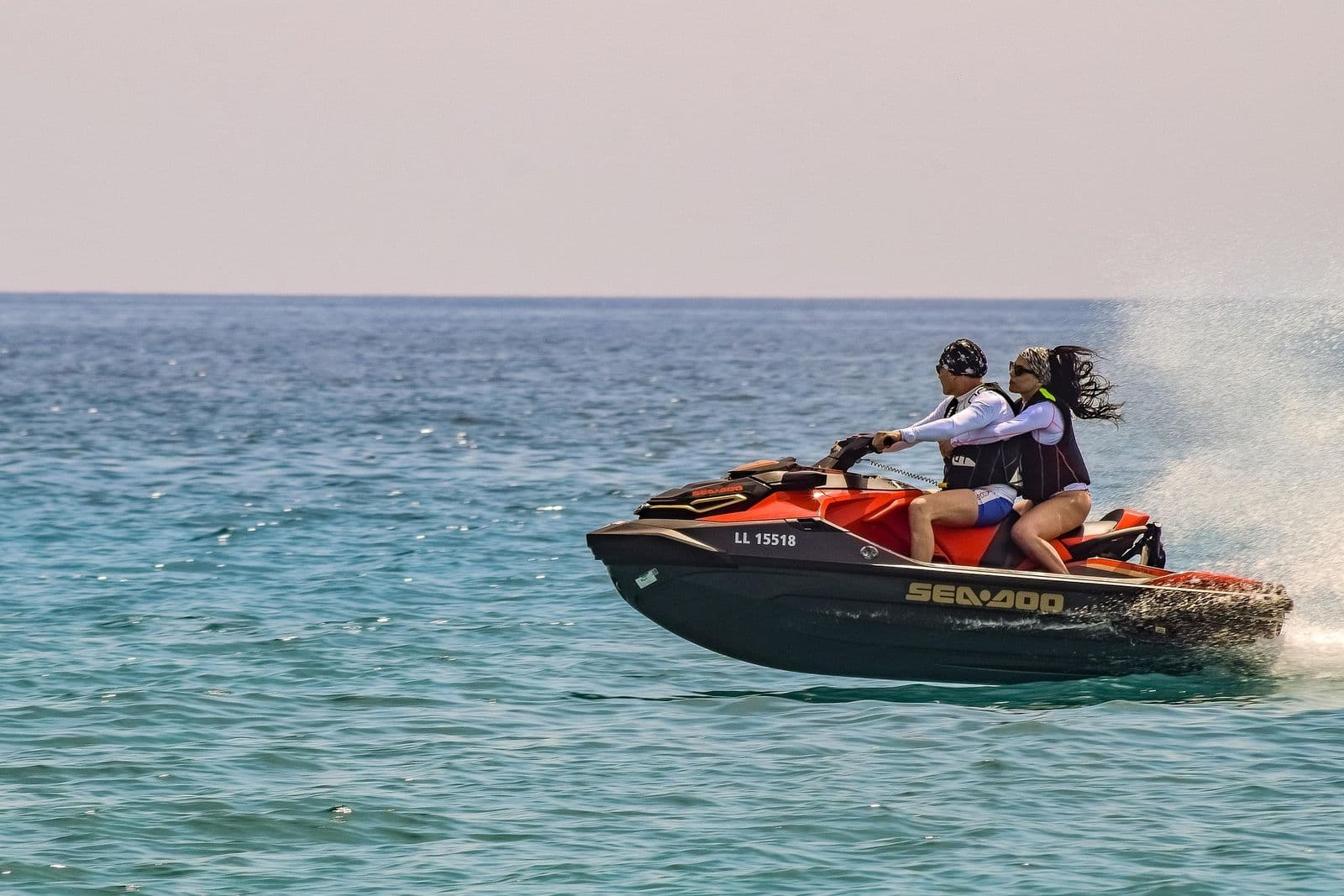Two riders on a personal watercraft, both wearing life jackets
